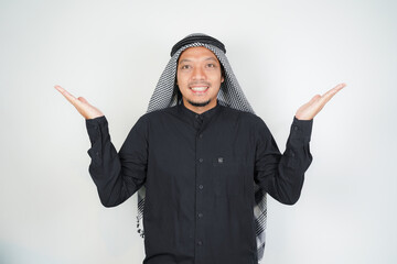 Cheerful Asian Muslim man wearing Arab turban sorban pointing hand finger at empty space on isolated