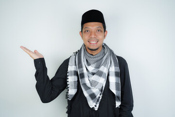 Cheerful handsome Asian Muslim man wearing Arab turban sorban pointing hand finger at empty space...