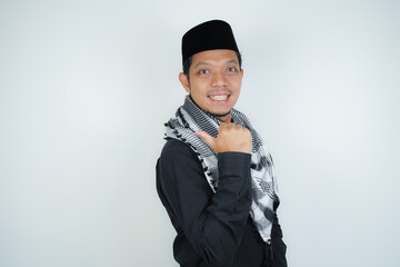 Cheerful handsome Asian Muslim man wearing Arab turban sorban pointing hand finger at empty space...