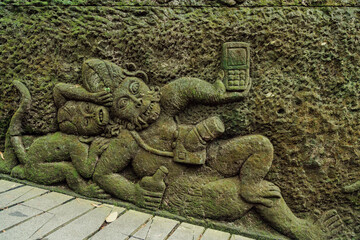 Relief carving of Monkey with mobile phone in Monkey Forest. Ubud, Bali, Indonesia.