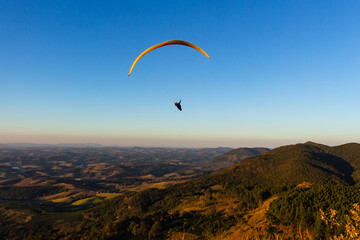Paraglider na hora dourada - POÇOS DE CALDAS, MG, BRAZIL - JULY 22, 2023:  Paraglider flying in the late afternoon with the sunlight making a beautiful gold color on the mountains.