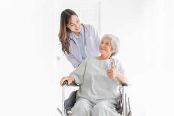 Asian doctor drive a wheelchair, old patient show thumb up sign with hand, doctor and old female talk about symptoms and treatment plan, rehabilitation activity, elderly healthcare promotion