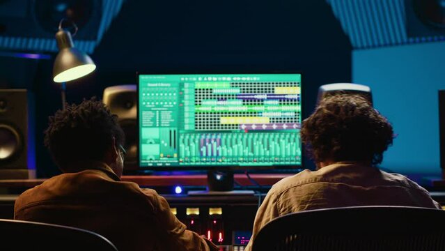 Diverse team of artist and sound designer working on editing tunes for a new hit, operating mixing console with moving faders and colored meters. Musician and producer making tracks. Camera A.