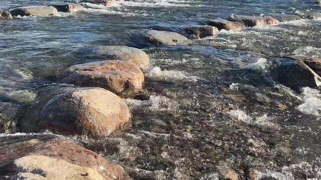 Clean river flows over boulder rapids in bright sunshine
