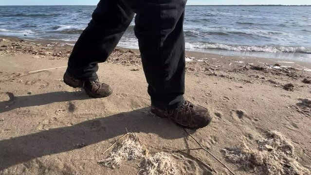 Low-level closeup of person walking on a beach near a wavy lake