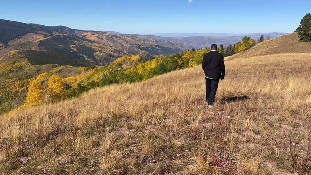 Following shot of a black man walking through a dry grassy mountain meadow