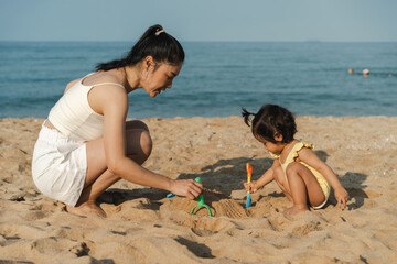 happy toddler baby girl playing sand toy with mother on the sea beach