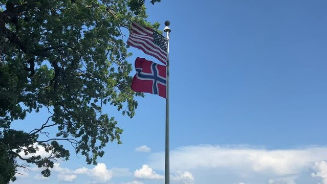 American and Norwegian flags fly together in a brisk breeze against a blue sky