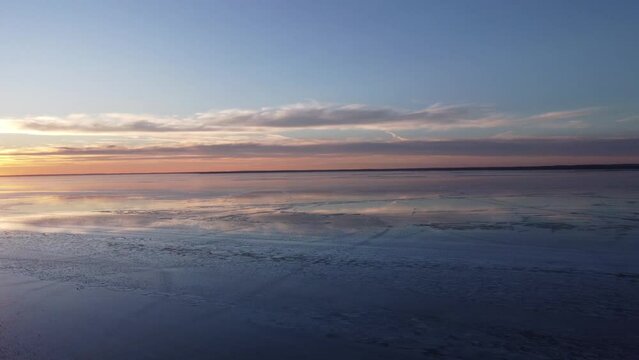 Aerial pan across a colorful winter sunset over an icy lake