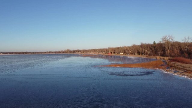 aerial pan out from sandy shore across partially frozen lake