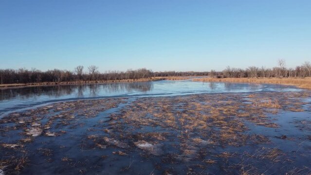 Flying over icy marsh and frozen lake with swans in distance