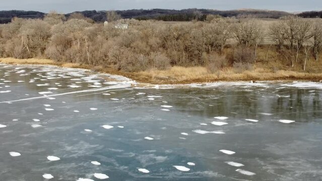 Aerial tilt down shot of frozen lake, rural farmland and forest