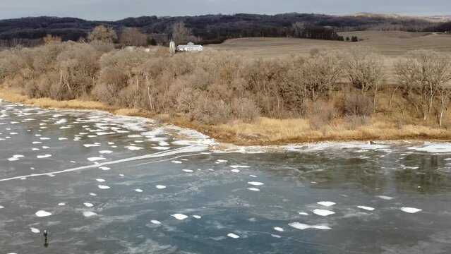 Aerial shot of rural frozen lake, forest and farmland in winter