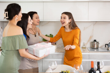 Excited young woman in vibrant festive attire warmly hosting besties bringing unexpected...