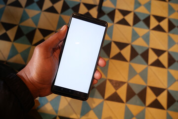 Person holding cell phone with blank screen on wooden flooring
