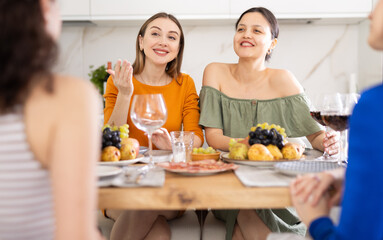 Obraz na płótnie Canvas Cheerful female friends enjoying home gathering with wine and light snacks at kitchen table, engaging in lively conversations..