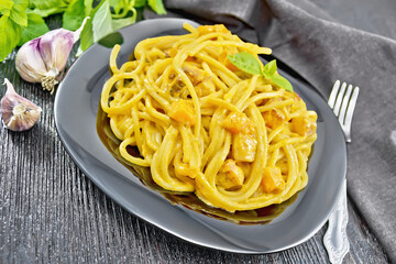 Spaghetti with pumpkin and bacon in plate on wooden board