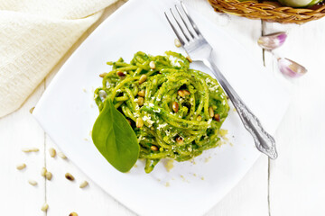 Spaghetti with spinach and pine nuts in plate on board top