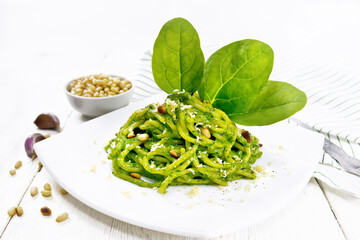 Spaghetti with spinach and nuts in plate on light board