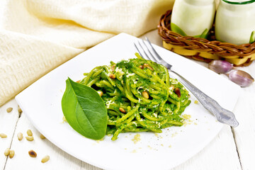 Spaghetti with spinach and pine nuts in plate on light board