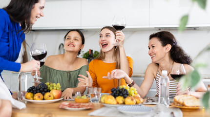 Obraz na płótnie Canvas Casual evening where group of cheerful carefree besties sharing wine, dining together, and chatting in cozy home kitchen ..