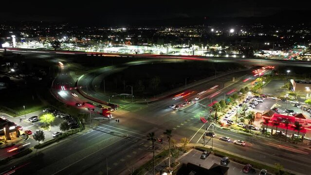 night time timelapse of the on-off-ramp on California Highway 10 Redlands Freeway merging with South Tippecanoe Ave in San Bernardino busy traffic long exposure headlights AERIAL DOLLY BACK RAISE UP
