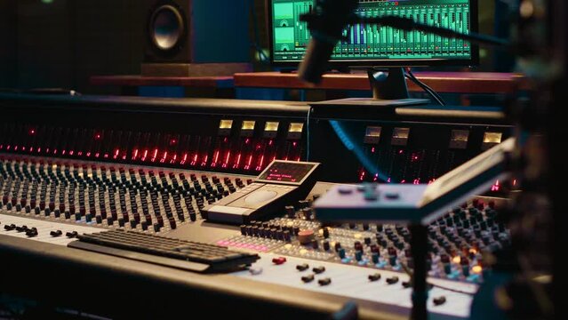 Control room with technical equipment and music recording software, professional studio editing and producing tracks. Audio console with moving faders and colored meters, high quality sounds.