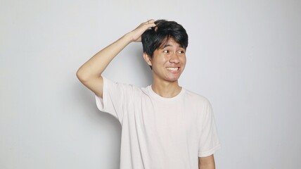 Young Asian man posing thinking while scratching his head like he is confused