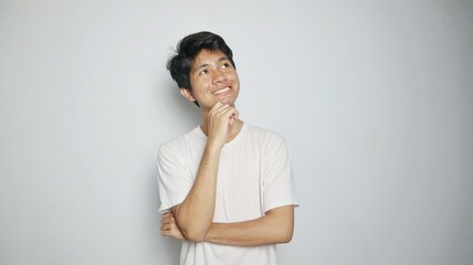 Young smiling Asian man thinking while looking up and hand holding chin