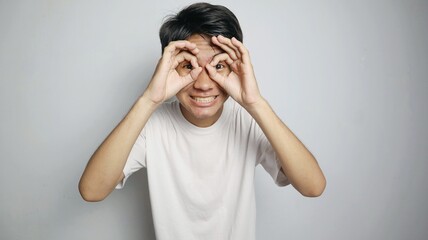 Asian young man poses making glasses using his hands and placing them like he is wearing glasses in...
