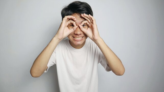 Asian young man poses making glasses using his hands and placing them like he is wearing glasses in front of his eyes