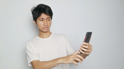 Asian young man astonished, strange, disgusted not wanting to see something on his smartphone