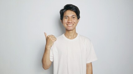 Happy smiling Asian young man pointing to the side or top with his thumb