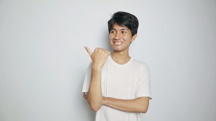 Happy smiling Asian young man pointing to the side or top with his thumb