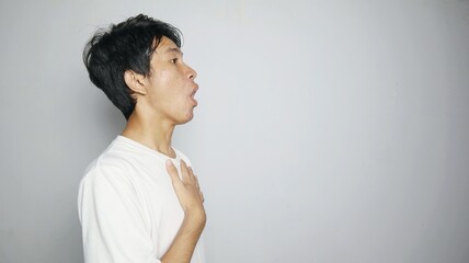 Side view of young Asian man in shock while holding his chest on an isolated white background