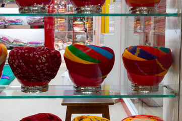 Display of modern turbans, headwear based on cloth winding with many variations, customary headwear for many. Bright, colorful men's costume displayed under glass show case. Jodhpur, Rajasthan, India.