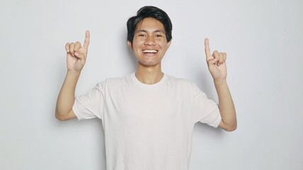 Excited young Asian man in white shirt pointing upwards
