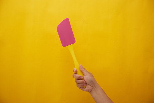 Photo of hand hold a spatula on yellow background 