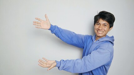 An excited young Asian man in a blue jacket pointing upwards with both hands
