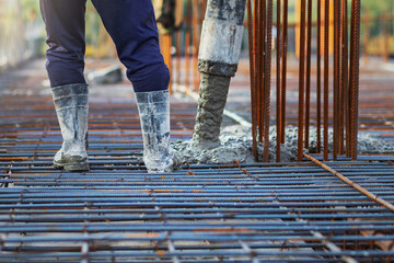 Concrete is being poured into a steel reinforcement frame at the construction site to form the structure's foundation or component.