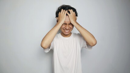 Young Asian man in white shirt gesturing with hand holding head, feeling dizzy, sick, stressed, depressed