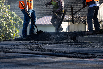 Steamroller compacting freshly load asphalt with pile of hot asphalt at end, residential road repaving construction project
