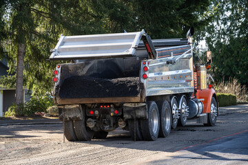 Dump truck with tailgate raised and filled with fresh hot asphalt ready to be fed into an asphalt paving machine, residential road repaving construction project  © knelson20