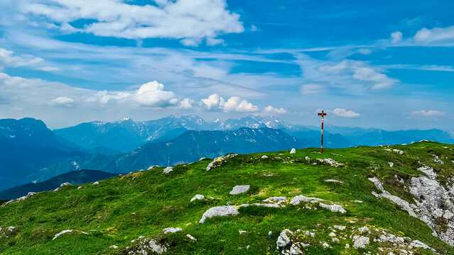 Sign indicating top of mountain peak Kriznik, Carinthia, border Austria Slovenia. Alpine meadow with scenic view of mountain range Karawanks, Slovenian Austrian Alps. Hiking trail on Petzen, Bleiburg