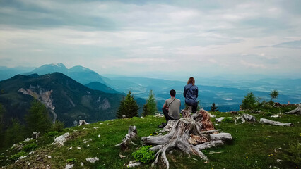 Hiker couple on alpine meadow near Feistritzer Spitze (Hochpetzen) with panoramic view of majestic mountain peaks Karawanks and Julian Alps, Carinthia, border Austria Slovenia. Hiking trail Petzen - obrazy, fototapety, plakaty