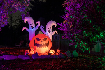 Glowing Halloween outdoor decorations of inflatable ghosts and pumpkins in purple light