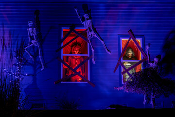 Halloween decorated house. Skeletons crawl along the blue wall towards the windows with monsters