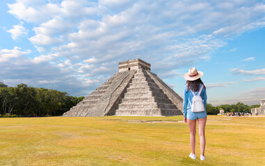 A beautiful woman in a white hat and mini jean shorts walks towards the pyramid -The pyramid of Kukulcan in the Mexican city of Chichen Itza in  the background - Mayan pyramids in Yucatan, Mexico