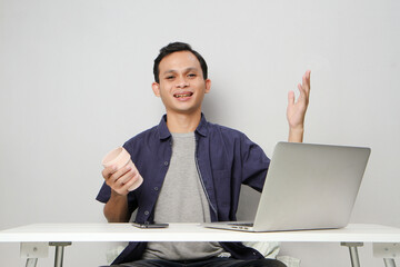 joyfull happy asian man at workplace while sitting in front of laptop computer. on isolated...