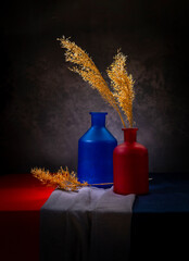 Bright still life with dry grass in a red bottle on a dark background